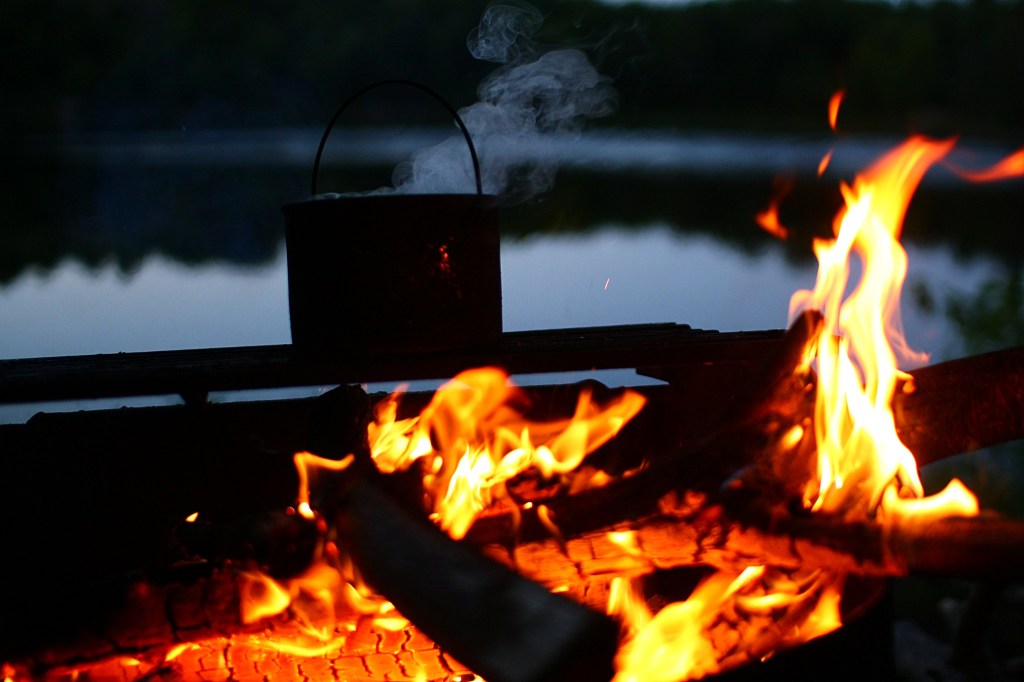 A bot of boiling water cooling next to an open fire.